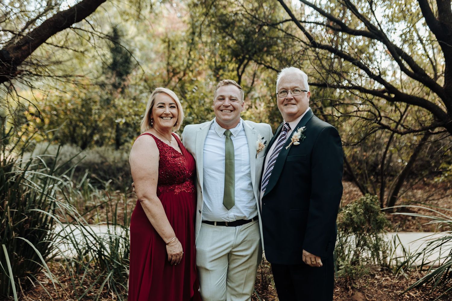 Wedding party in formal attire poses together outdoors with natural scenery in background.