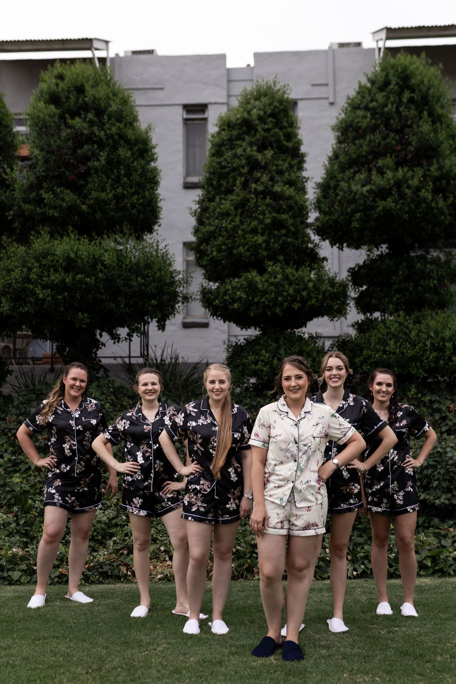 A coordinated group poses in matching dark floral outfits with one person in light attire on a lawn.
