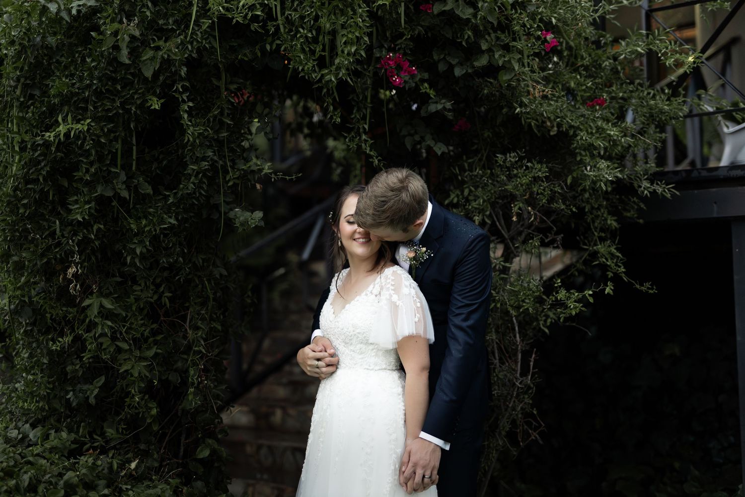 Intimate wedding moment captured in garden setting with climbing vines.