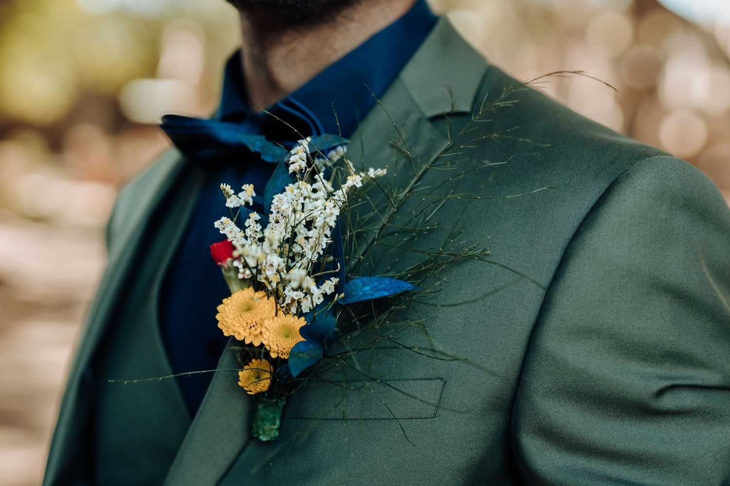 Close-up of yellow and blue floral boutonniere pinned to a dark green suit jacket.