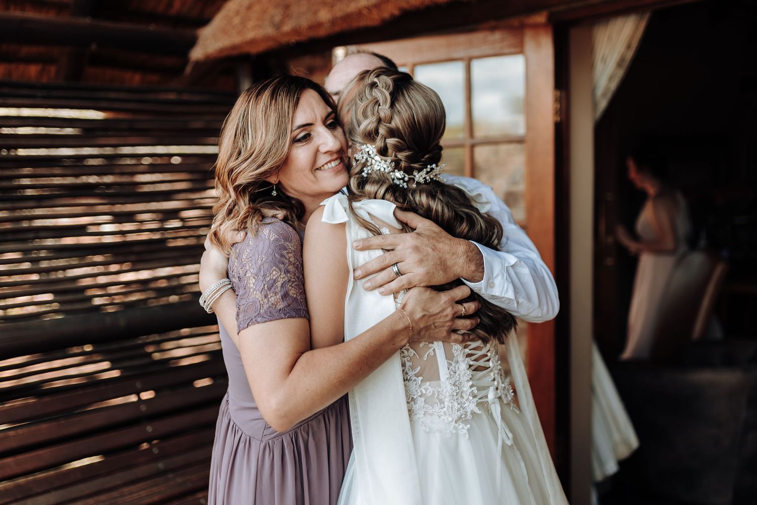 Emotional embrace between wedding party members in a rustic venue with natural lighting.