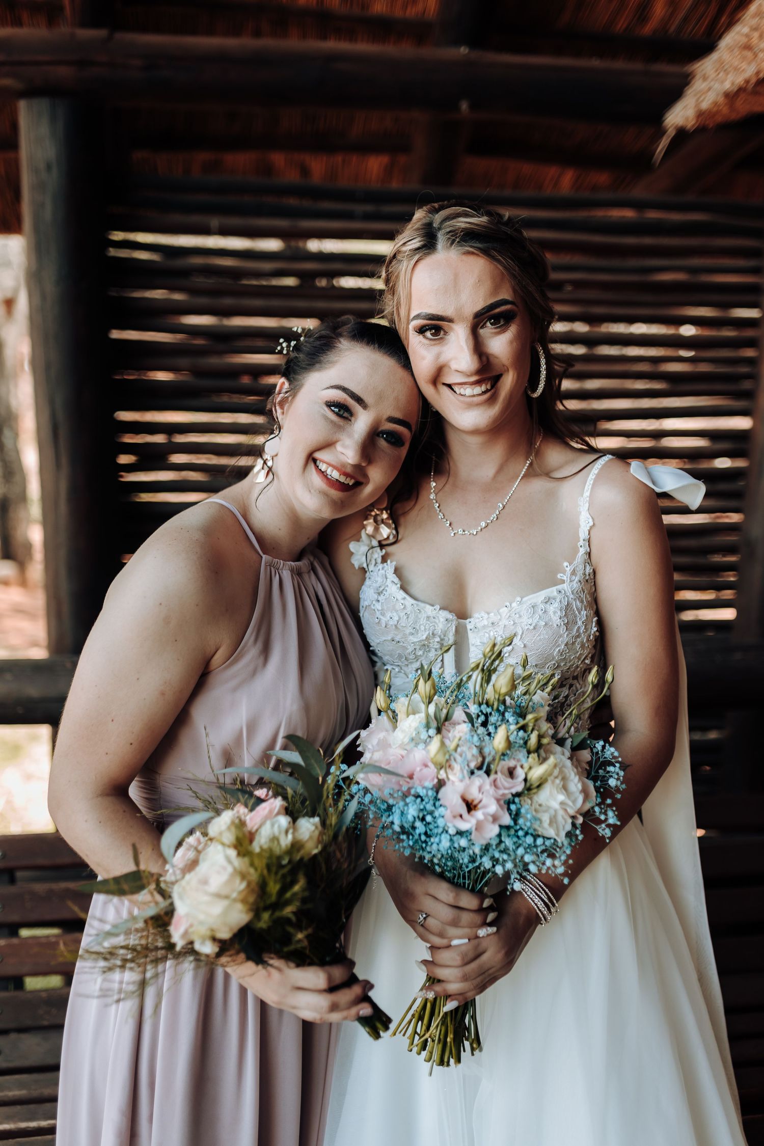 Wedding party portrait with bridesmaid in dusty rose dress and bride holding floral bouquets.