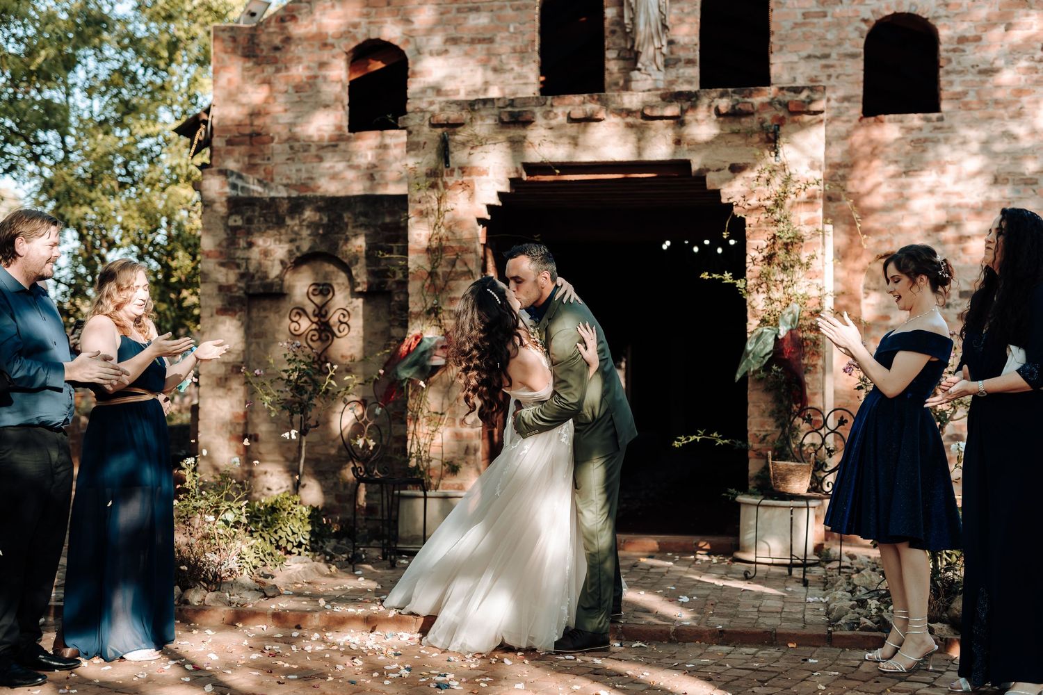 Newlyweds celebrate with guests throwing confetti outside a historic brick venue.
