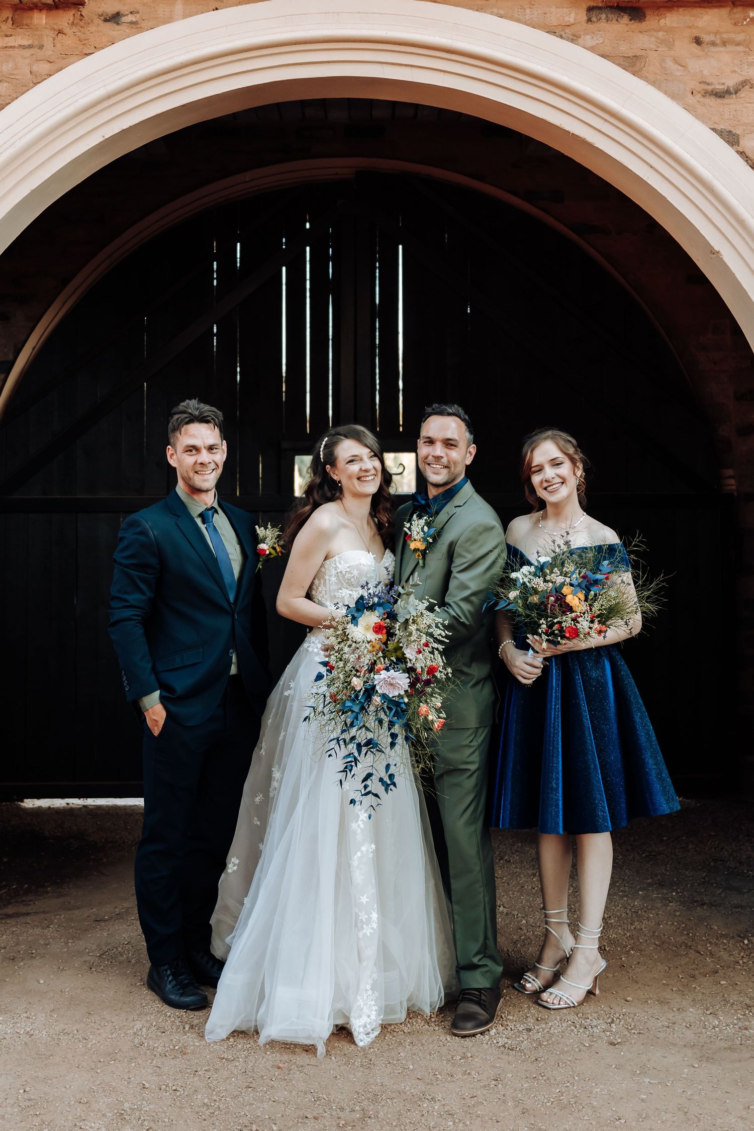 Formal wedding party portrait under stone archway featuring sage green and navy color scheme.