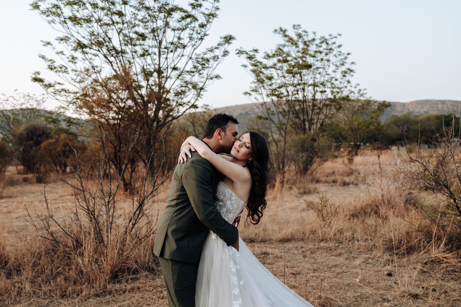 A romantic wedding couple embracing and kissing in a natural autumn landscape.