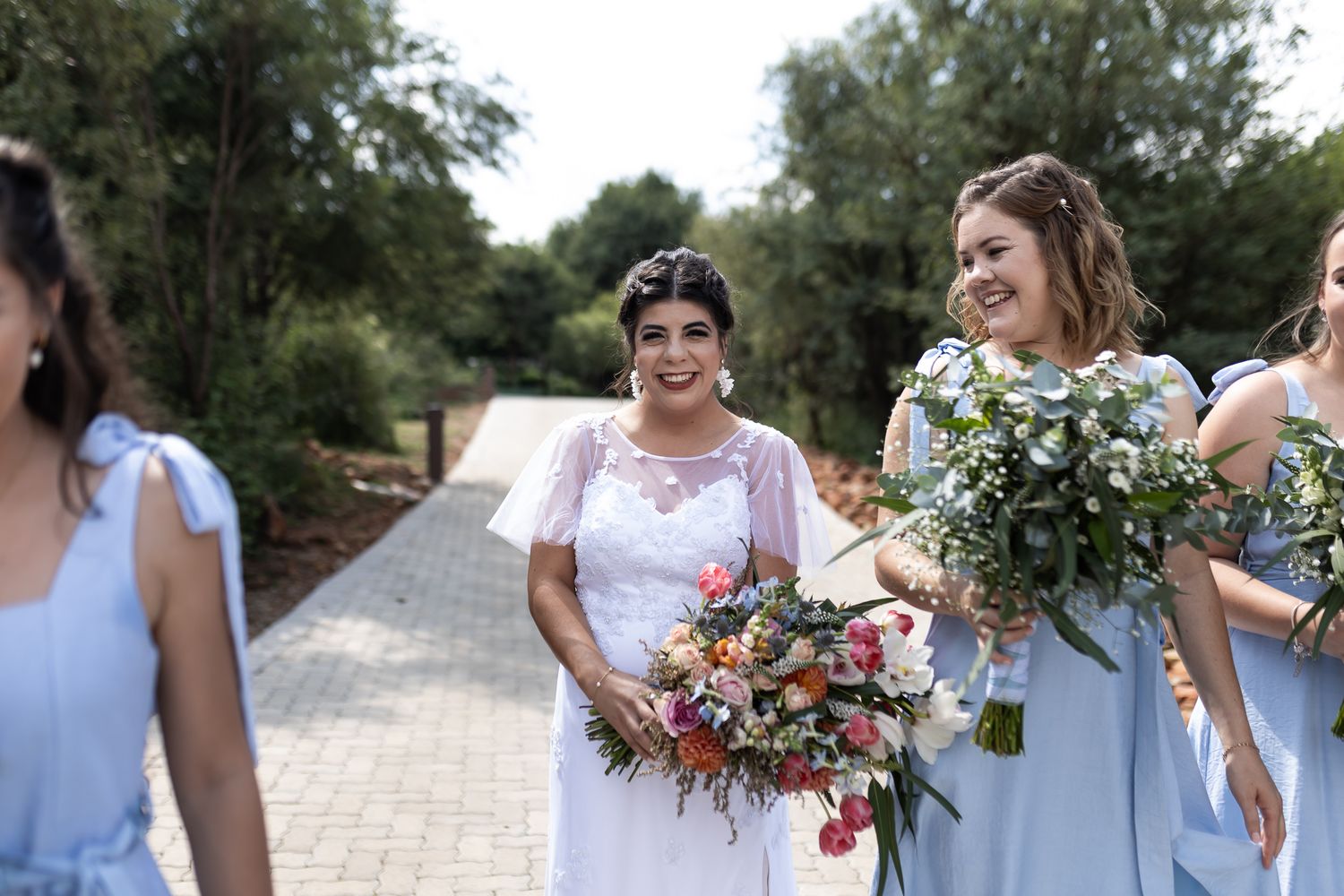 Bridesmaids in light blue dresses share joyful moments while holding vibrant floral bouquets.
