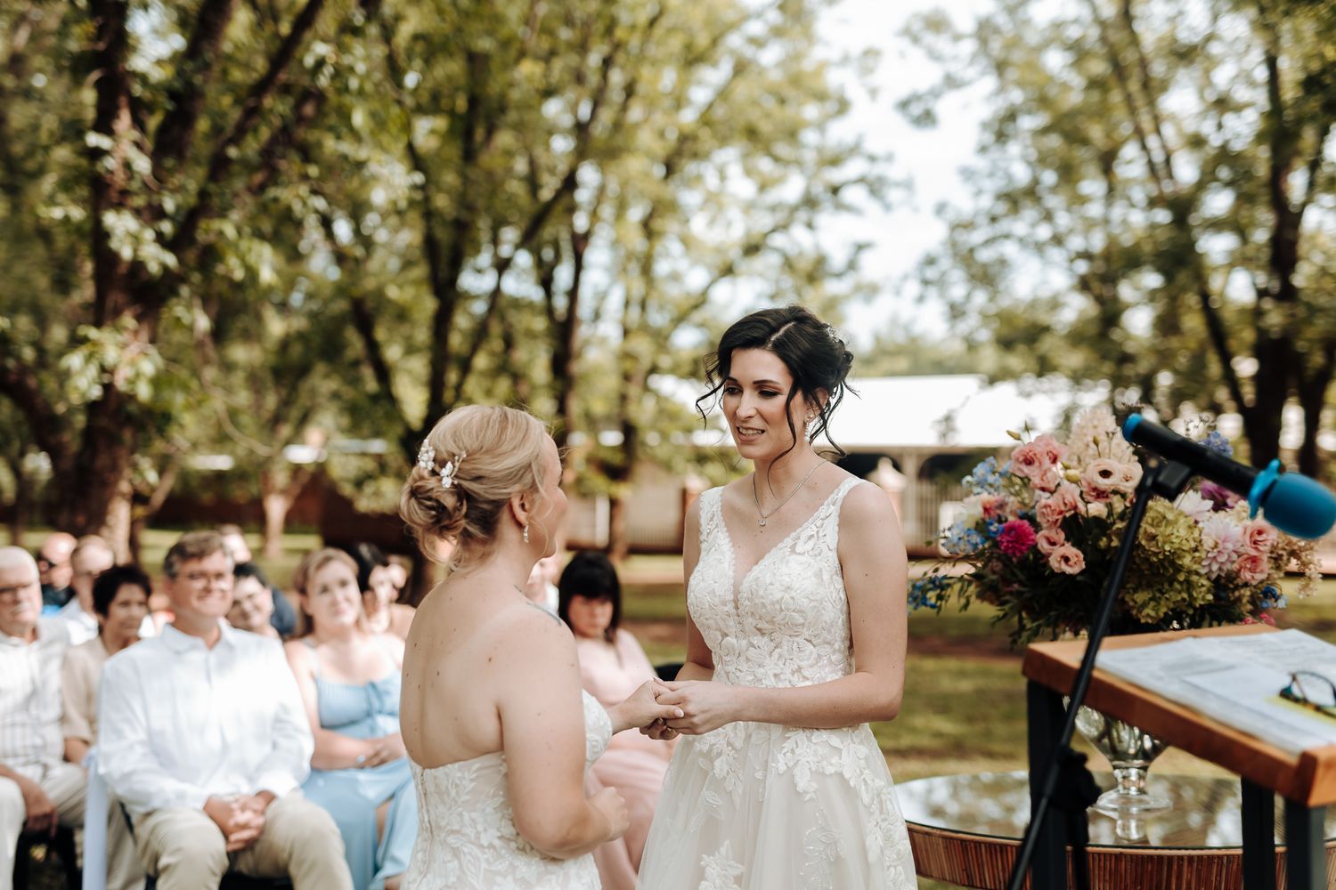 Wedding ceremony taking place in a sunlit garden with guests seated on white chairs.