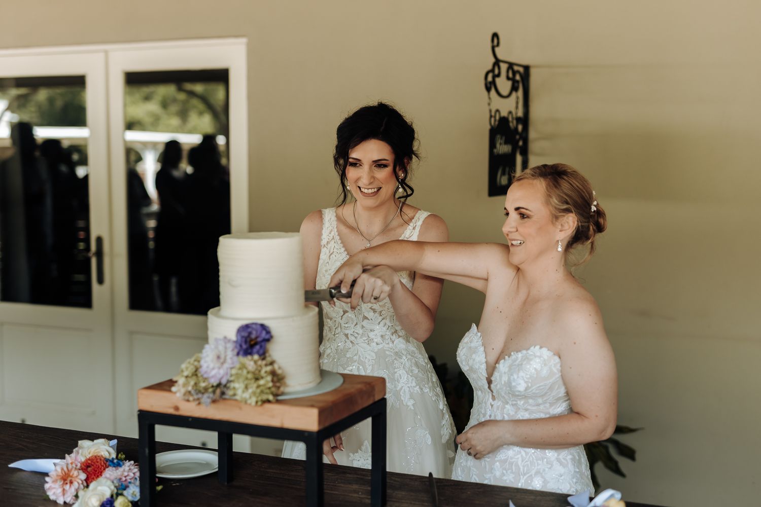 Two elegant wedding dresses on display next to a simple white and purple cake.