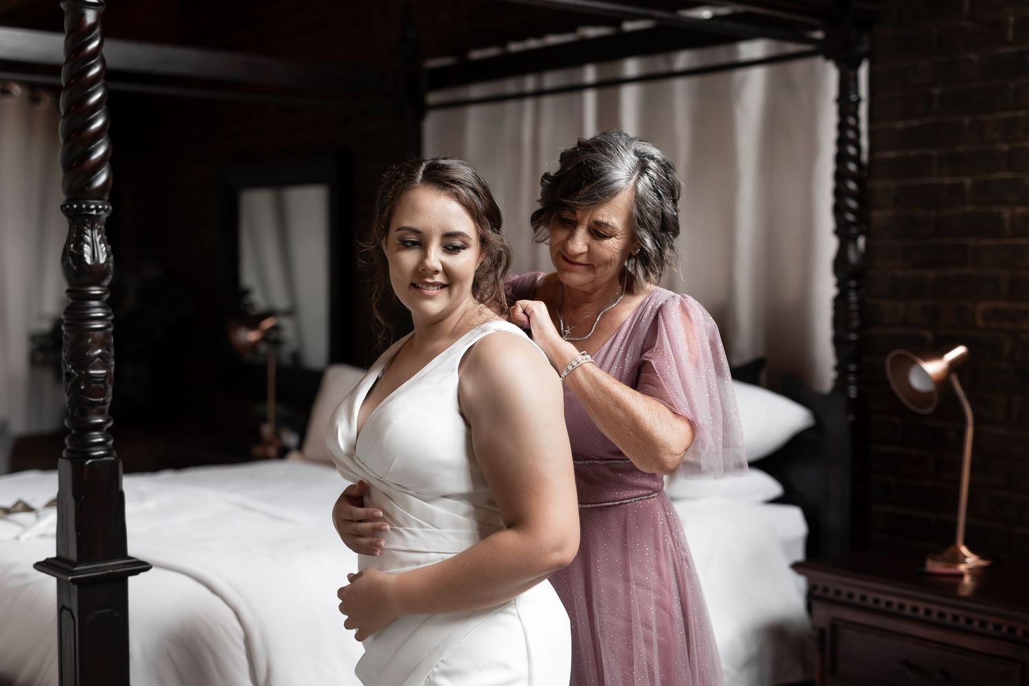 Final wedding dress adjustments in bedroom with romantic lighting.
