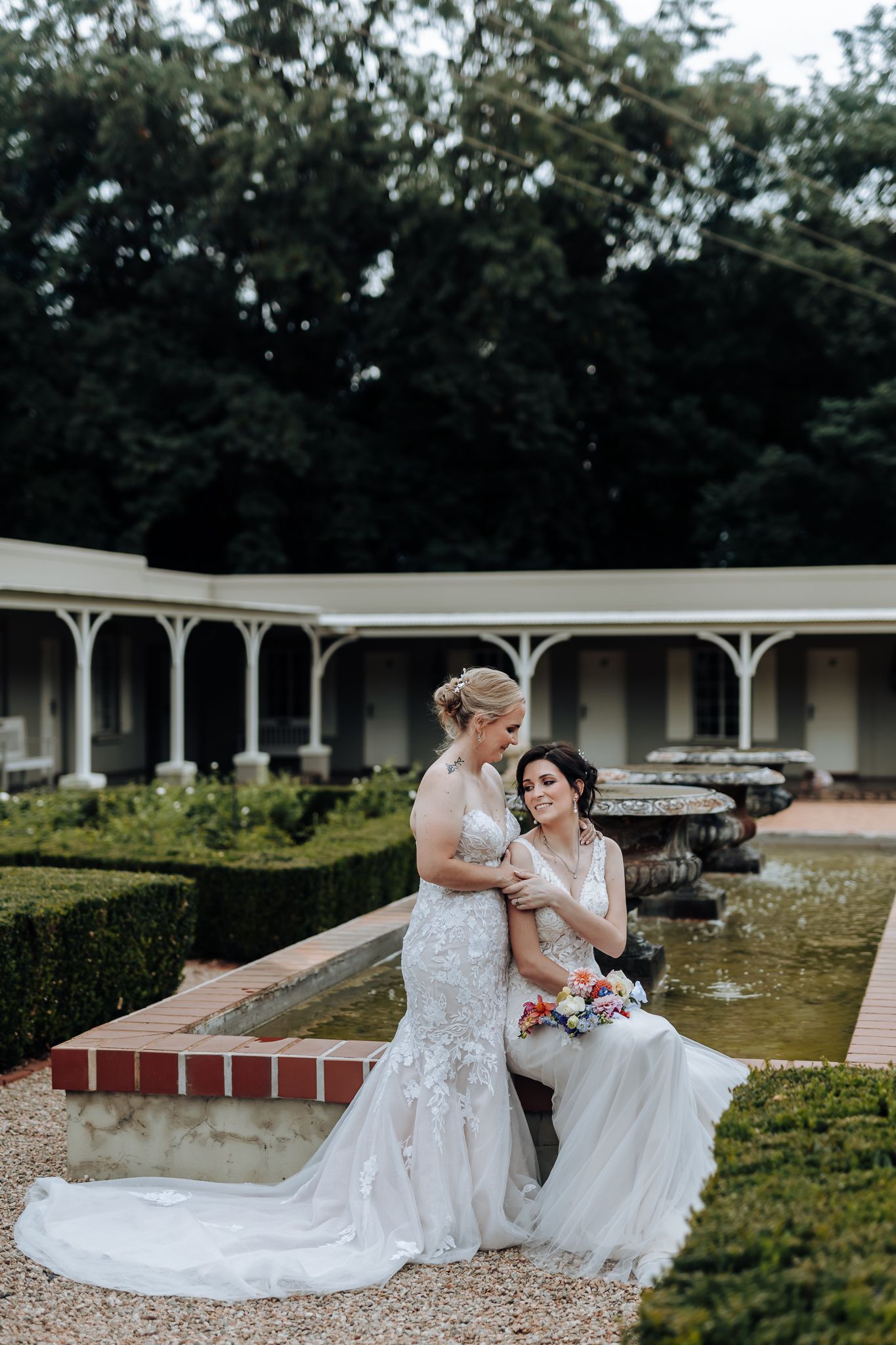 Wedding couple shares tender moment beside ornate garden fountain at historic venue.