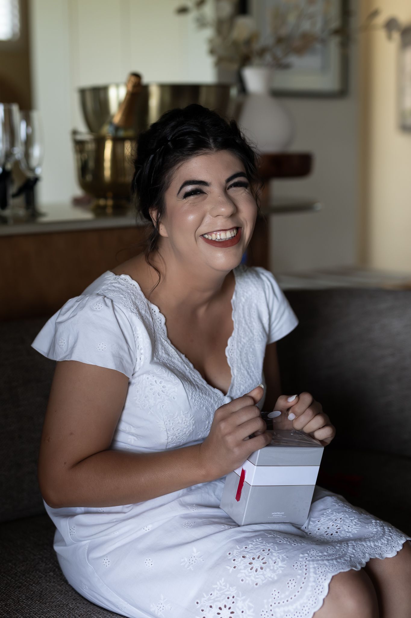 A person wearing a white dress smiles while sitting on a couch with a notebook.