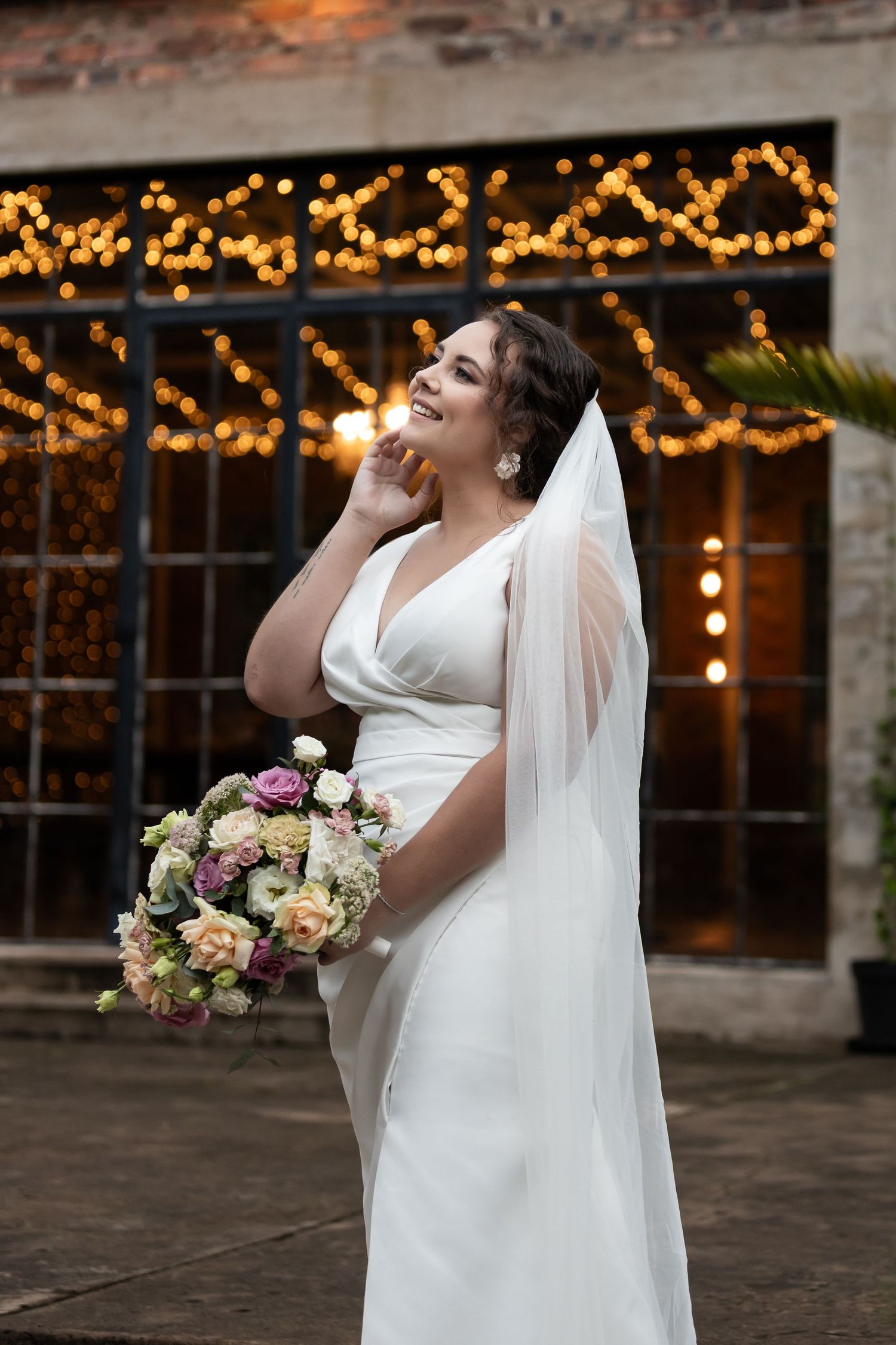 Joyful bridal portrait with string lights glowing in background at dusk.