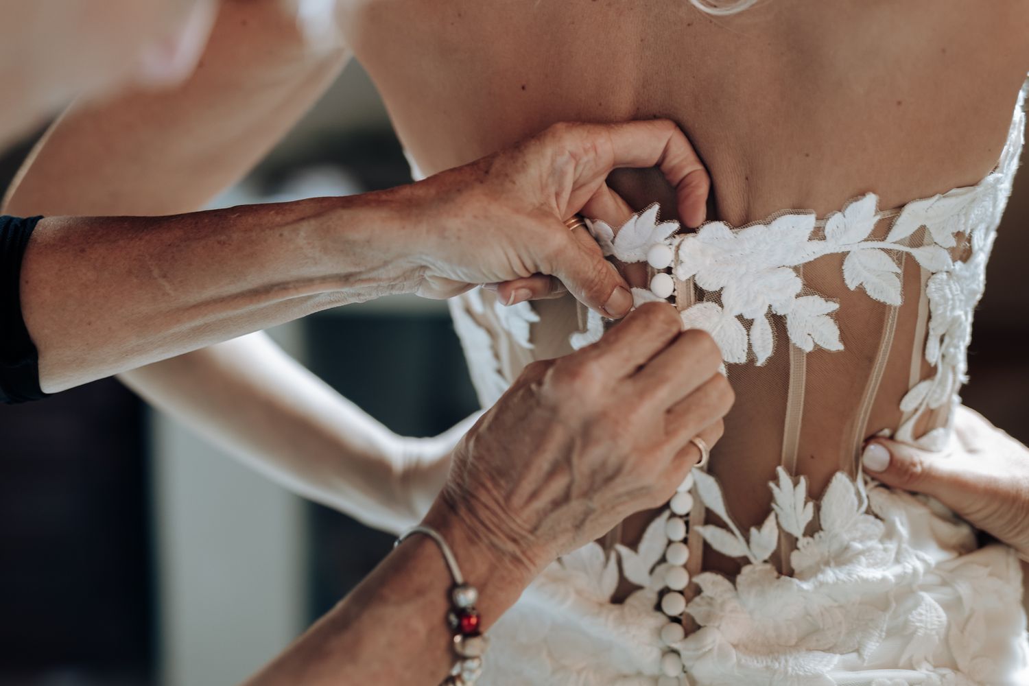Close-up view of hands adjusting delicate lace details on a white wedding dress.
