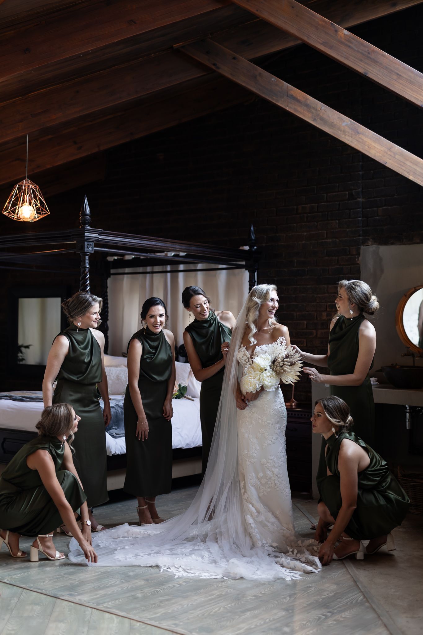 Wedding party gathers around to assist with the bride's dress in an atmospheric loft-style room.