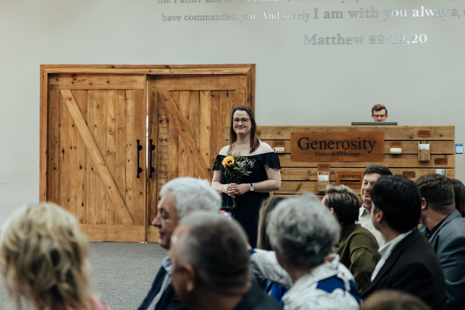Wedding guests gather in an indoor venue with wooden paneled walls and rustic decor.