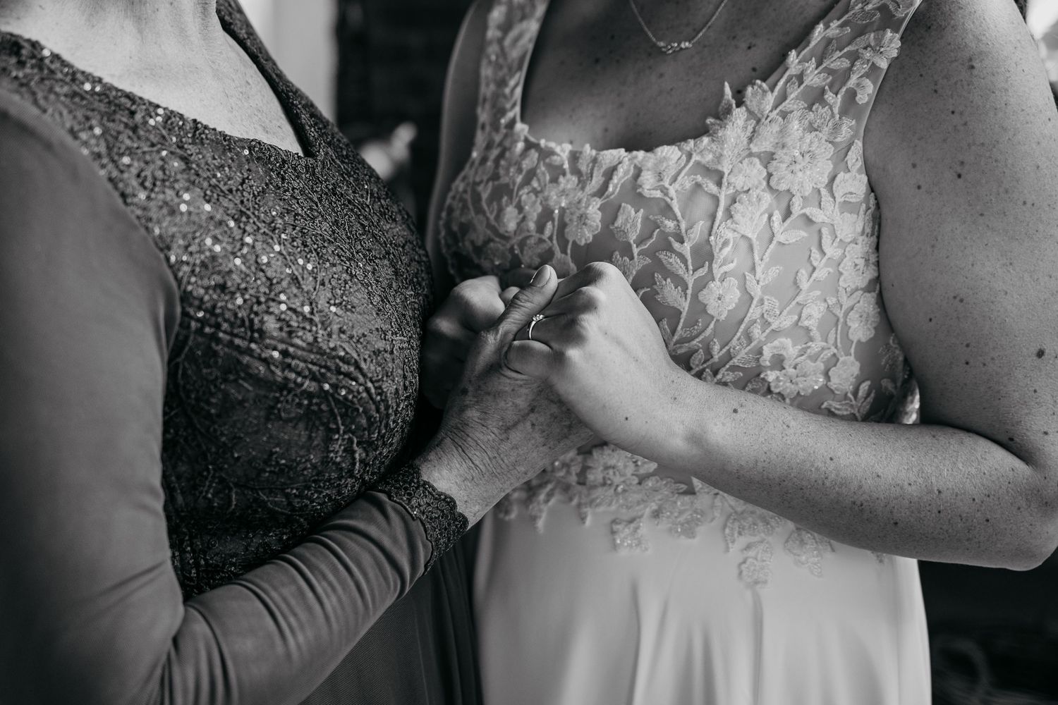 Black and white closeup of hands touching while wearing elegant lace dresses during an intimate moment.