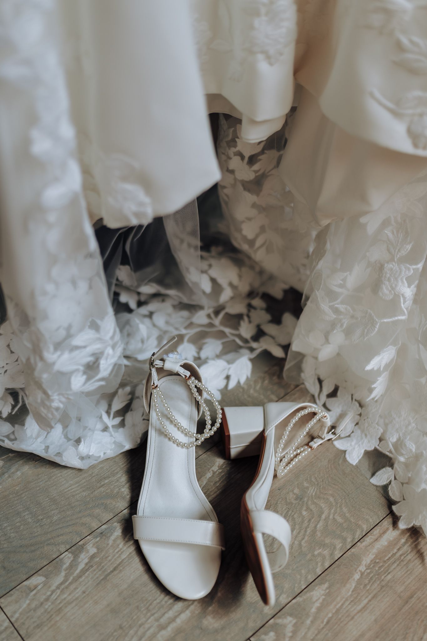 White wedding sandals with pearl straps placed beneath flowing lace wedding dress details.