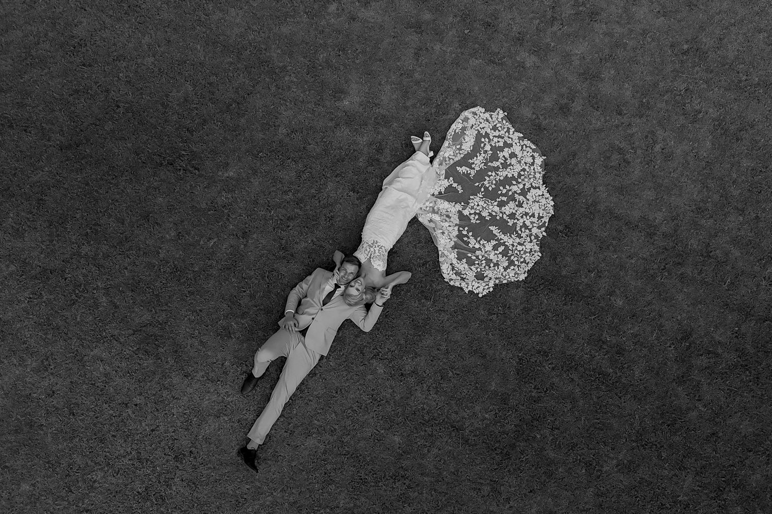 Aerial drone shot of a wedding couple lying on dark ground, creating artistic contrast with the dress.