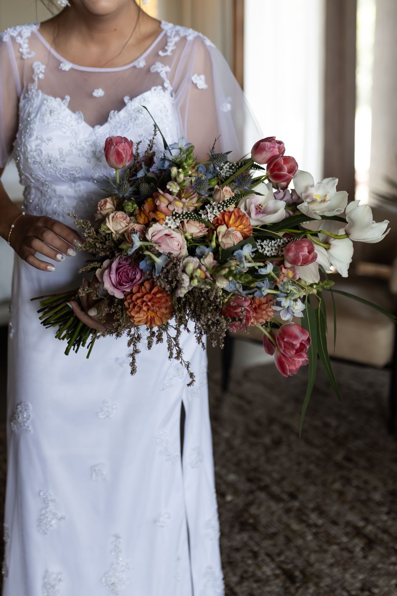 A stunning bridal bouquet with pink and red flowers against a white lace wedding dress.