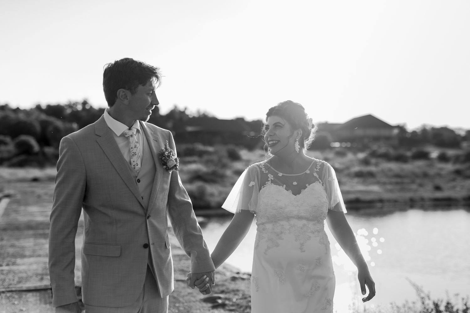 Couple holding hands while walking along waterfront in black and white photo.