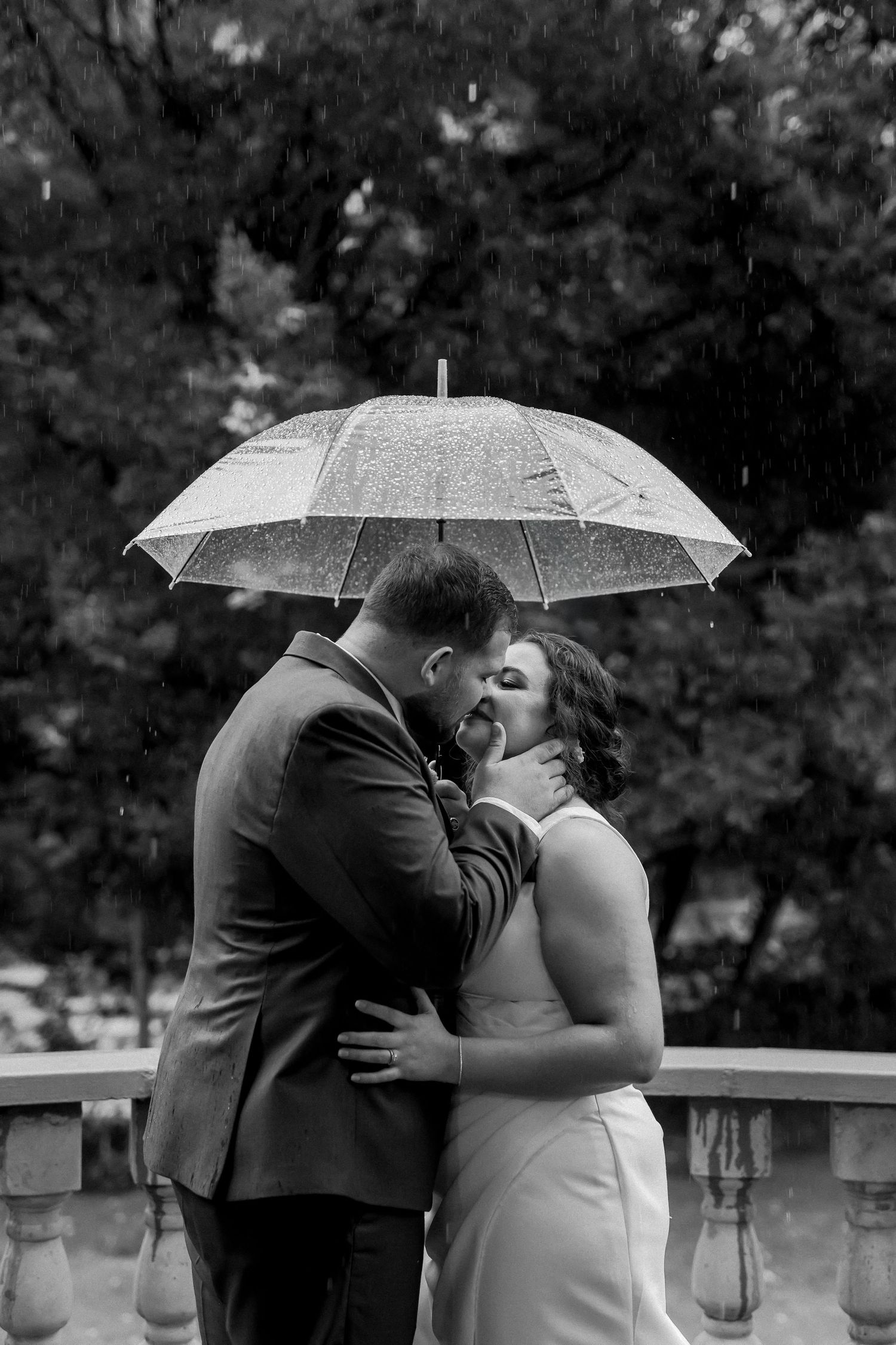 Black and white intimate portrait of couple beneath clear umbrella on stone terrace.