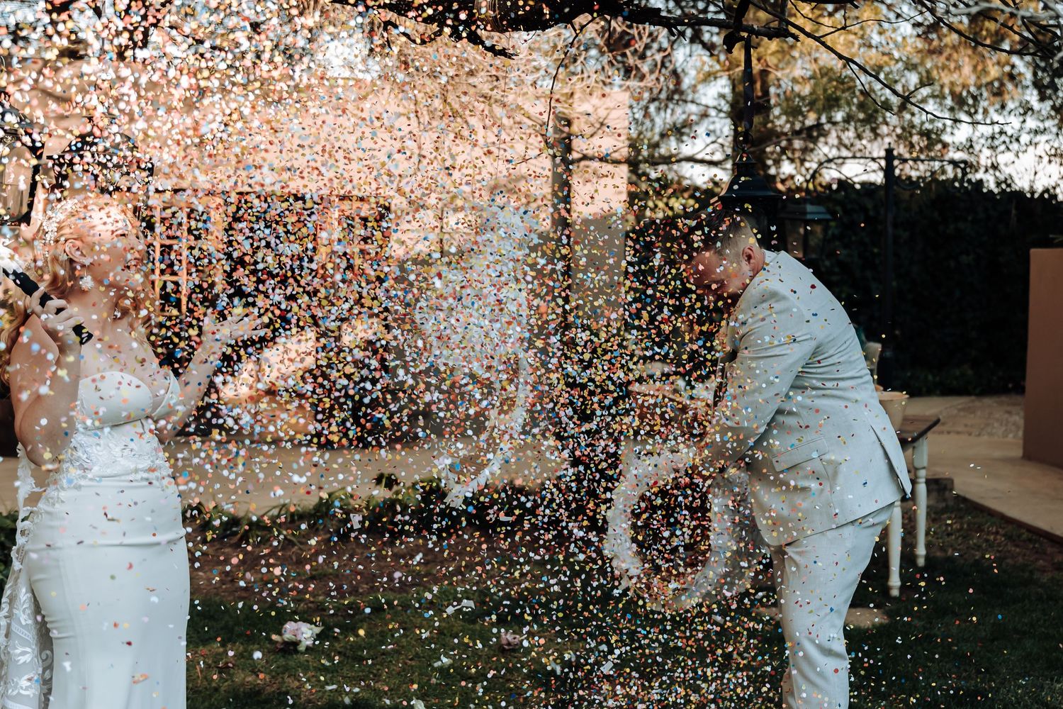 Champagne spraying during an outdoor wedding celebration creates a sparkling moment against garden backdrop.