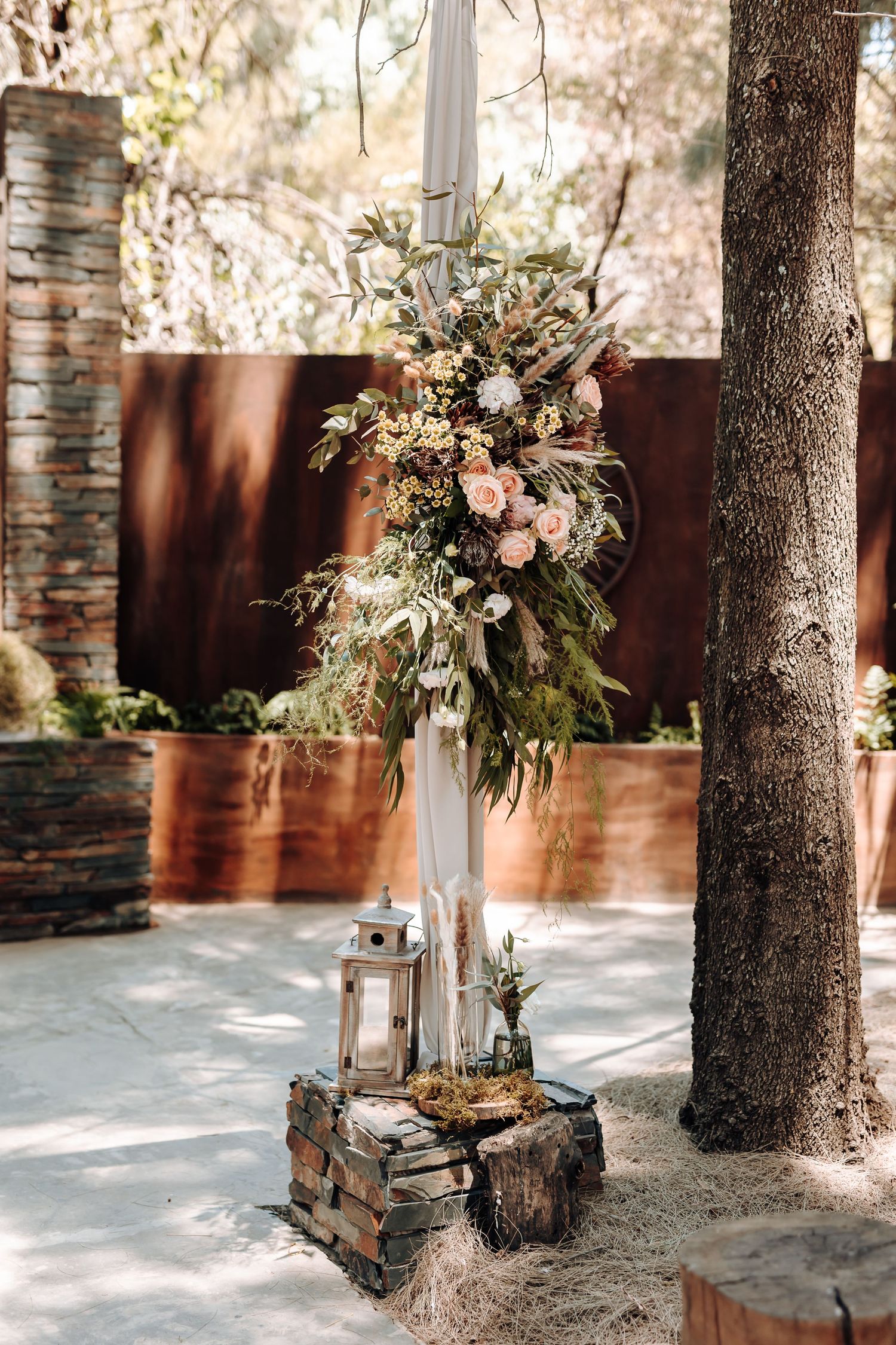 Rustic wedding decor featuring floral arrangement on stone pedestal with lantern accent.
