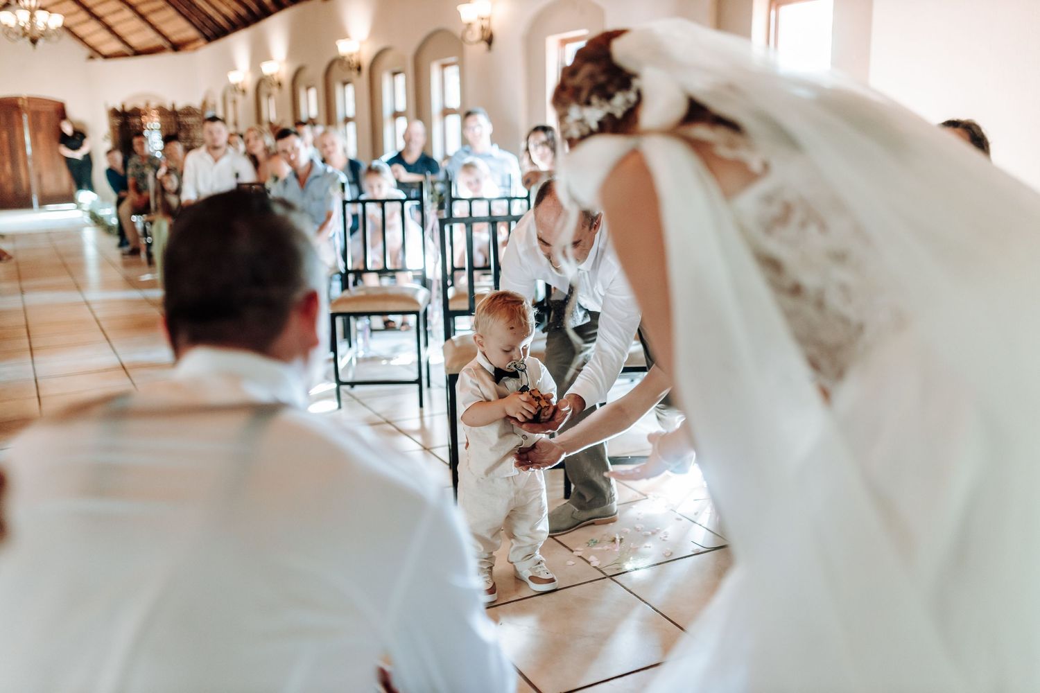 Young child participates in wedding ceremony while guests look on in rustic venue.