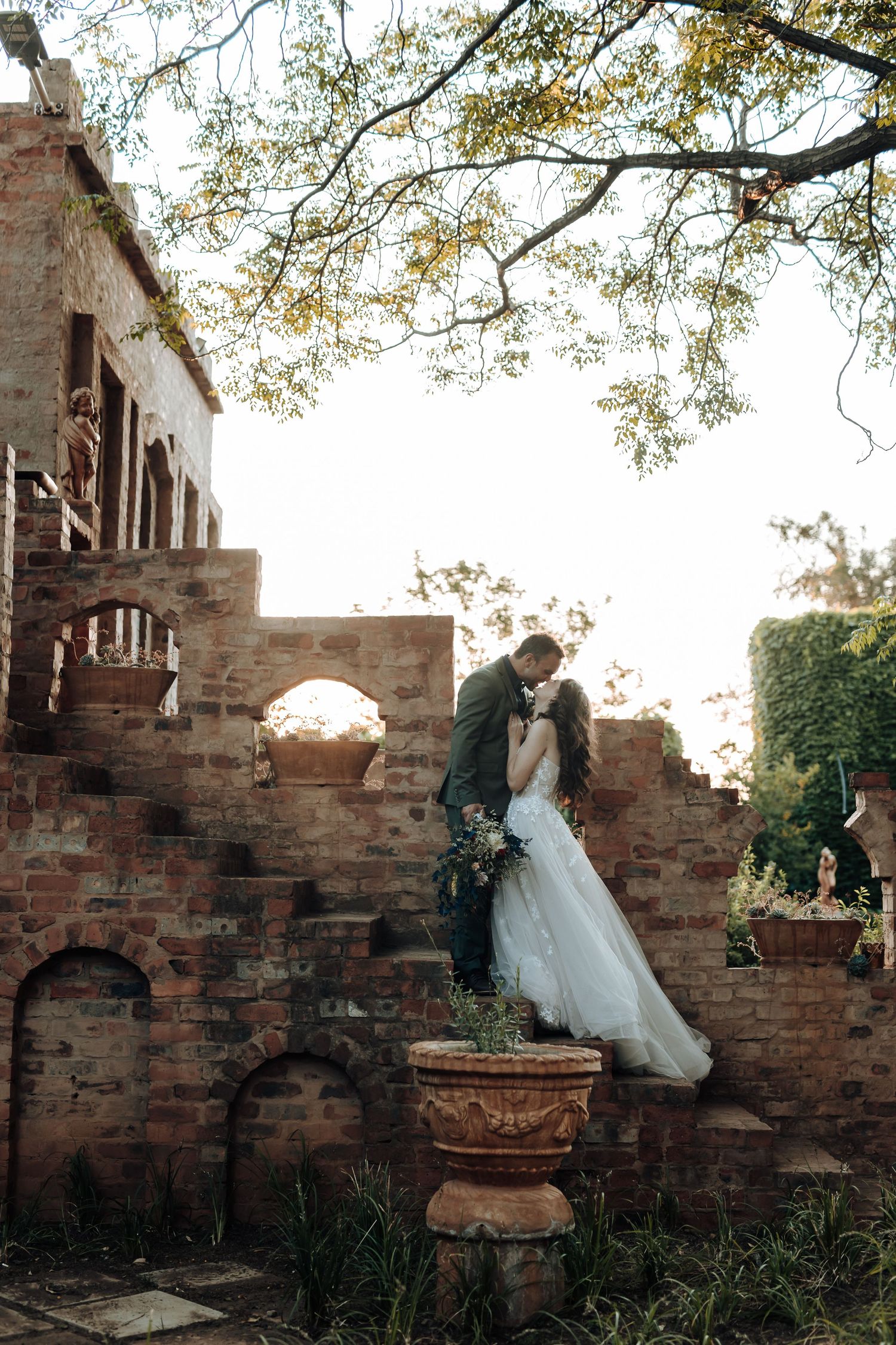 A romantic wedding photo on rustic brick steps with a white gown and autumn foliage overhead.