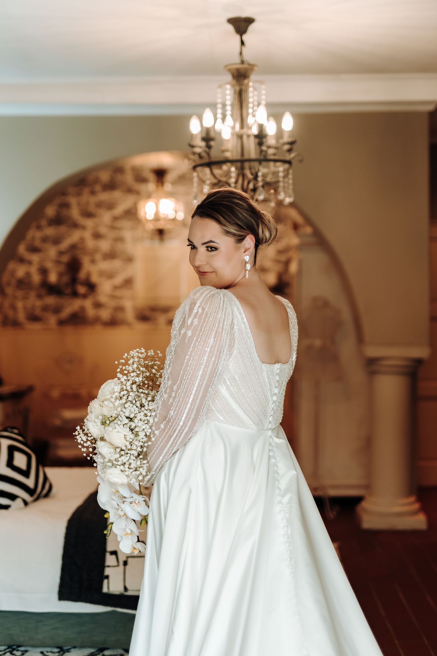 Back view of wedding gown showing elegant button details and sheer sleeves against stone archway.