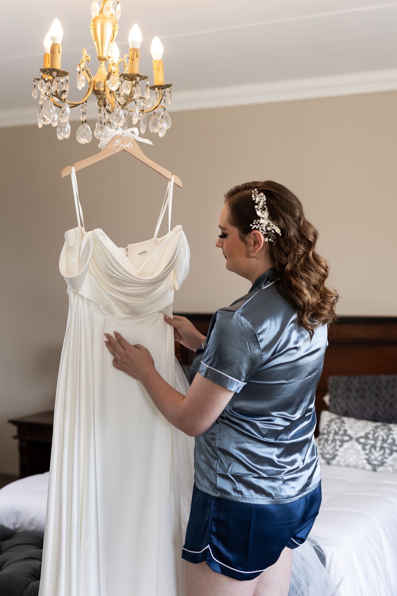 Wedding dress preparation with crystal chandelier and blue silk pajamas.