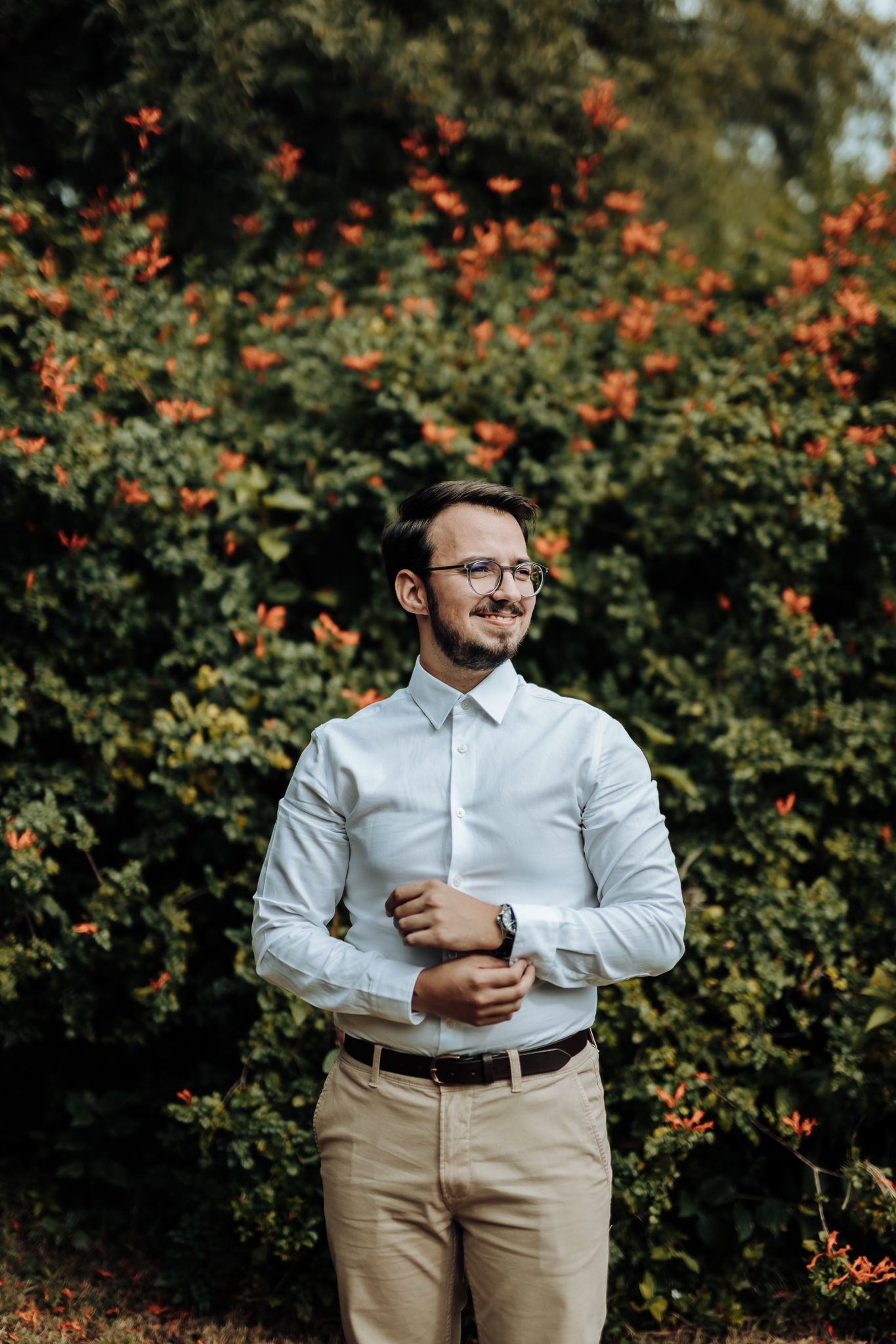 Portrait of groom in crisp white shirt against backdrop of orange flowering bushes.