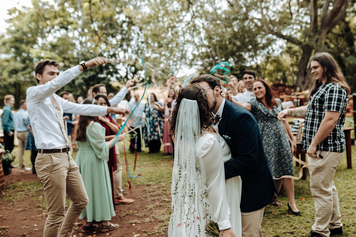 Wedding guests form an arch with their arms while the newlyweds walk beneath during an outdoor celebration.