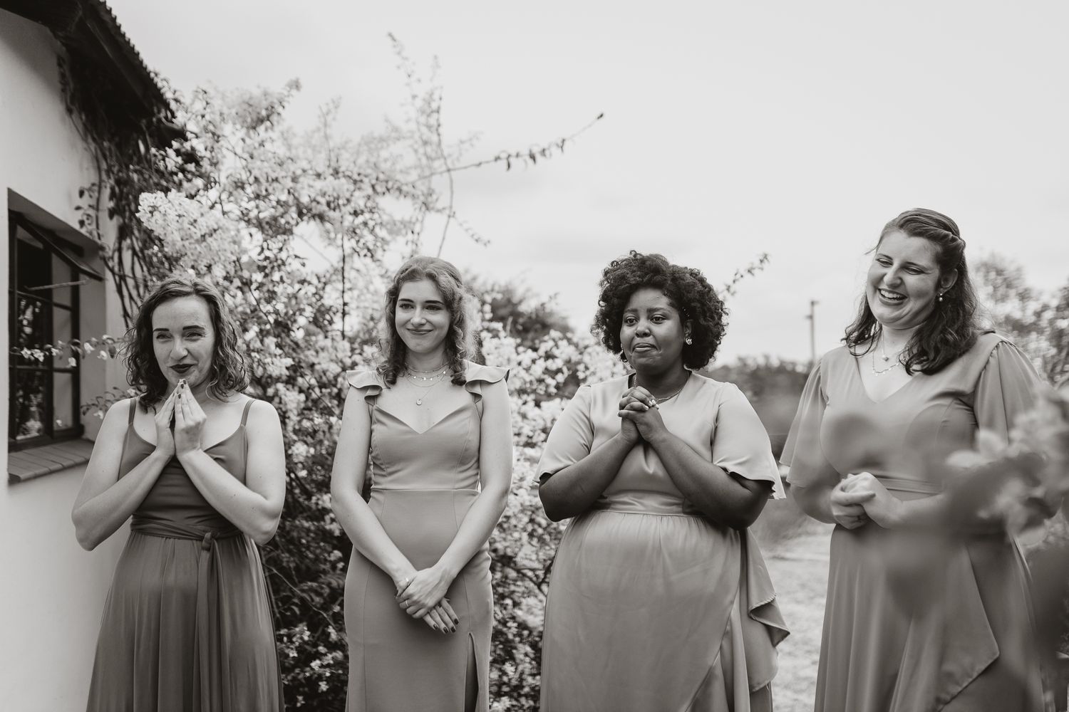 Black and white photo of bridesmaids showing surprised expressions at outdoor wedding.