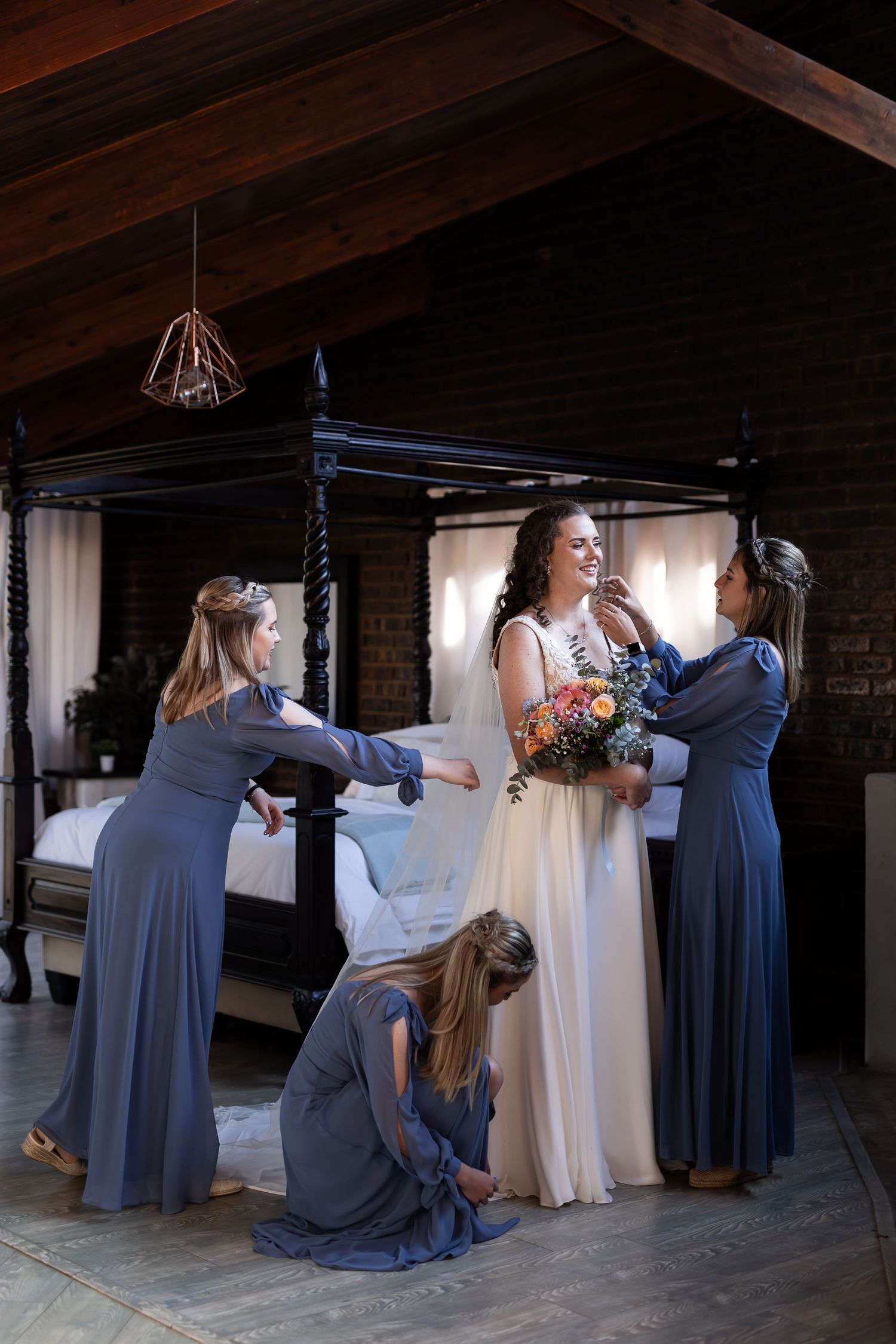 A bridal party helps a bride into her wedding dress during a getting ready moment in a rustic venue.