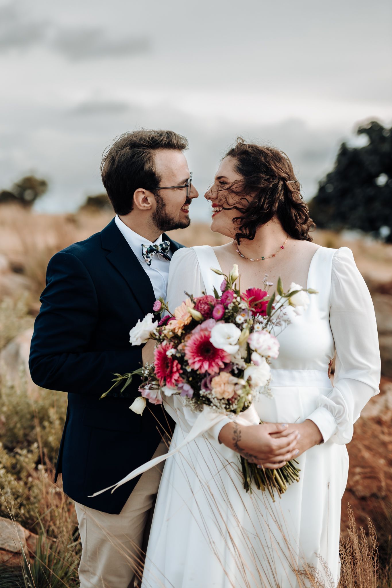 Close-up portrait of couple with pink and white bouquet in rustic outdoor setting.