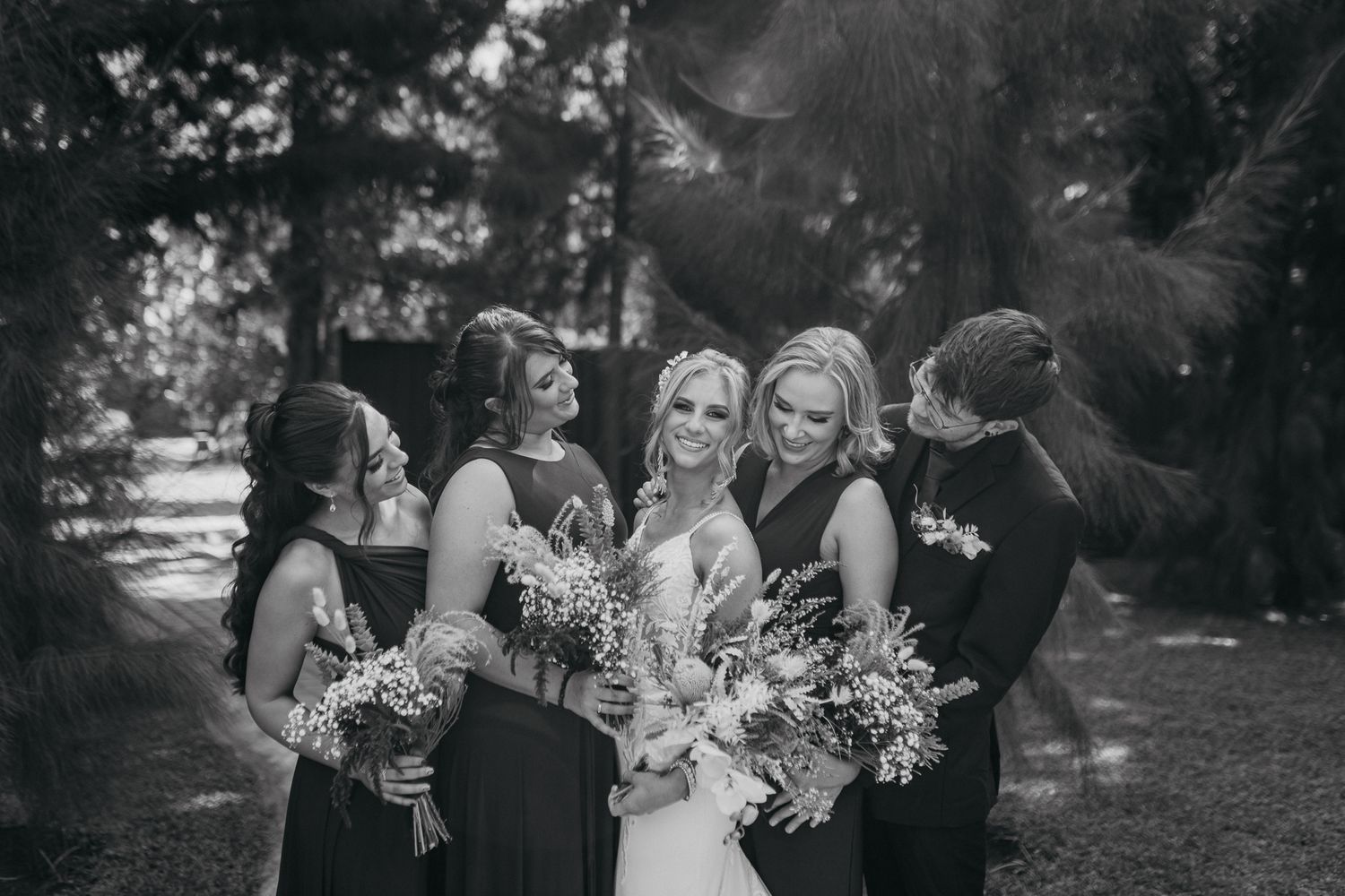 Black and white photo of wedding party gathered together outdoors with bouquets.