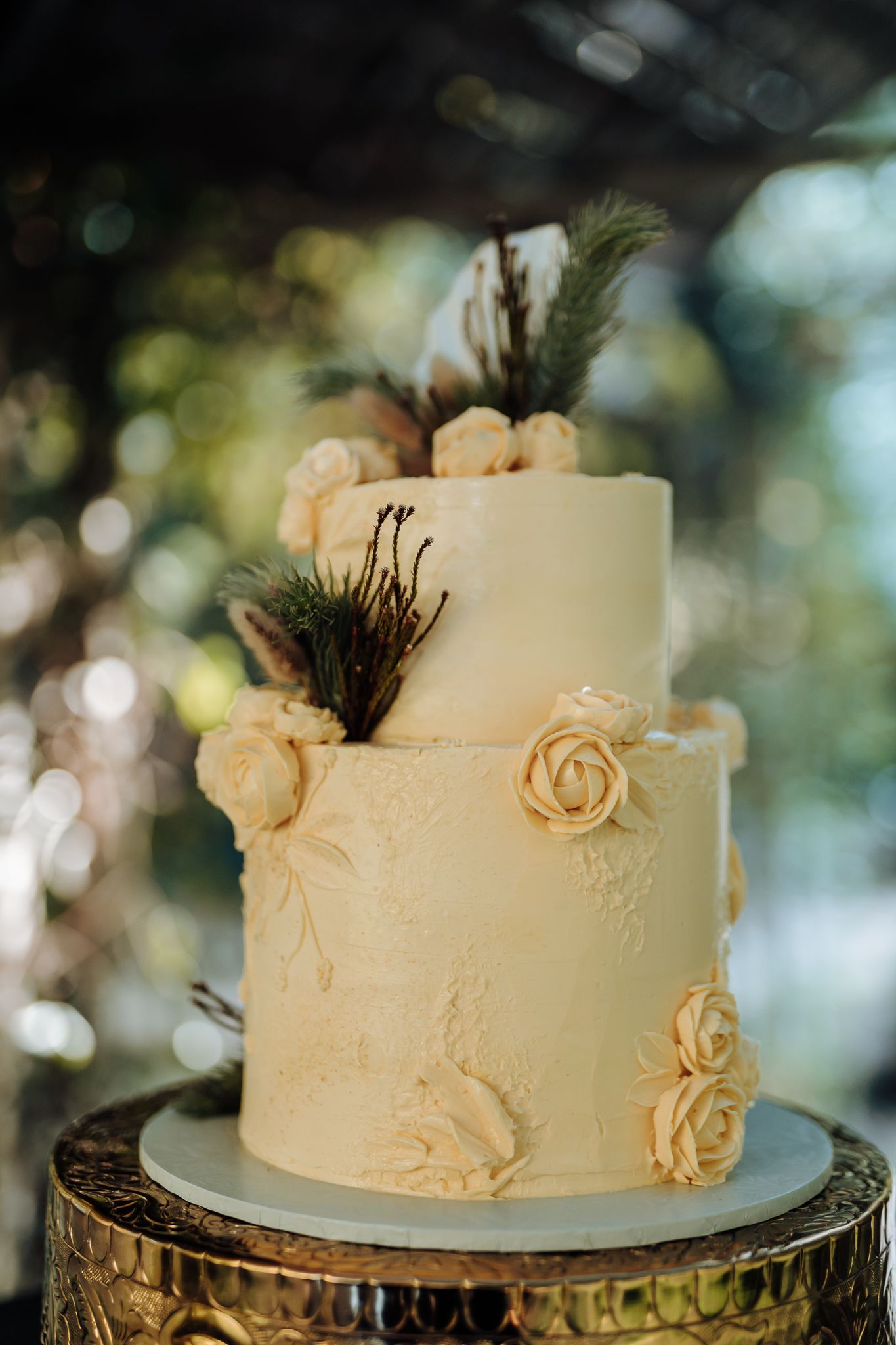 Elegant two-tier white wedding cake decorated with cream roses and pine accents.