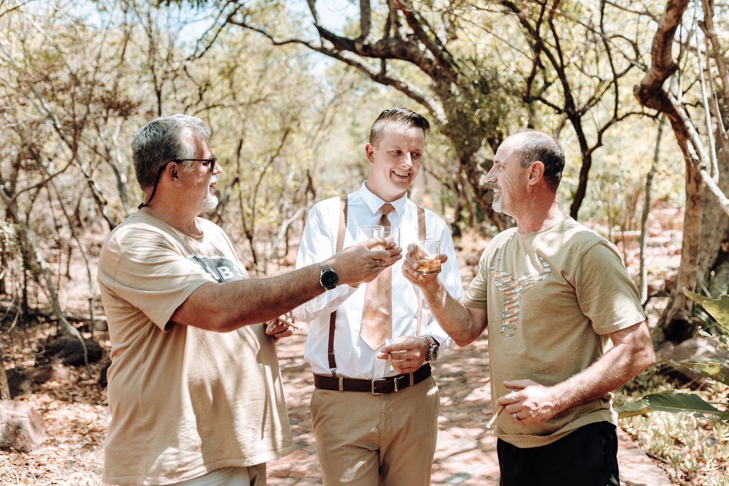 Three people in casual formal wear toasting with drinks outdoors.