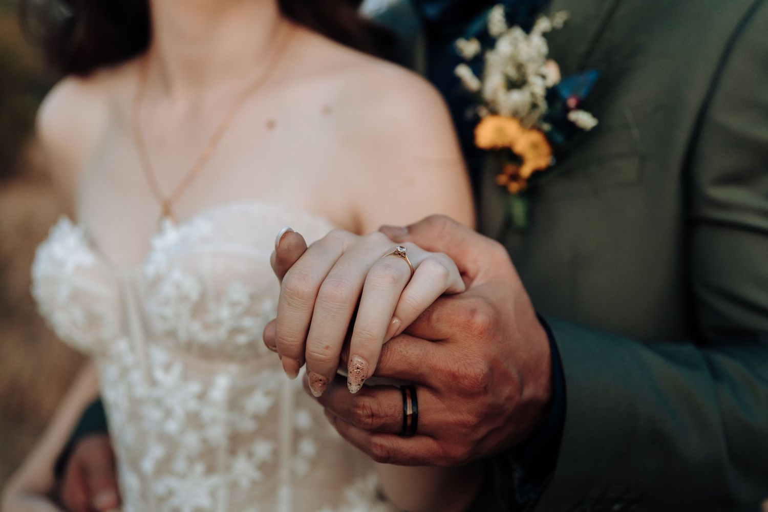 Detailed shot of newlyweds holding hands, showing wedding dress details and formal attire.