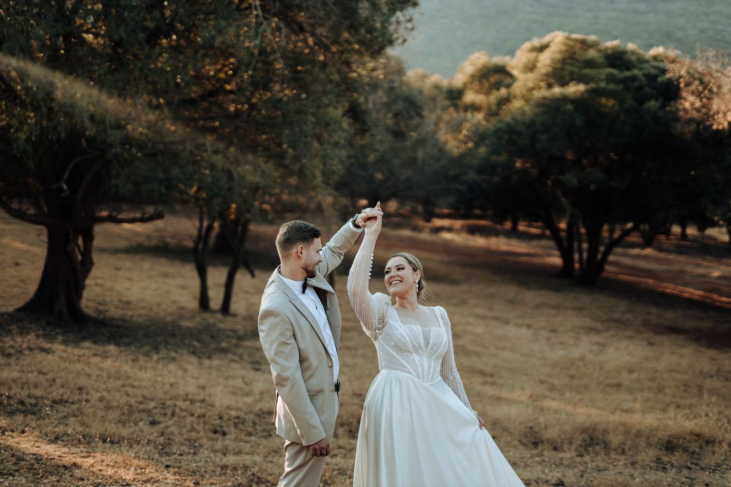Wedding couple dancing in an outdoor setting with golden sunlight filtering through trees.