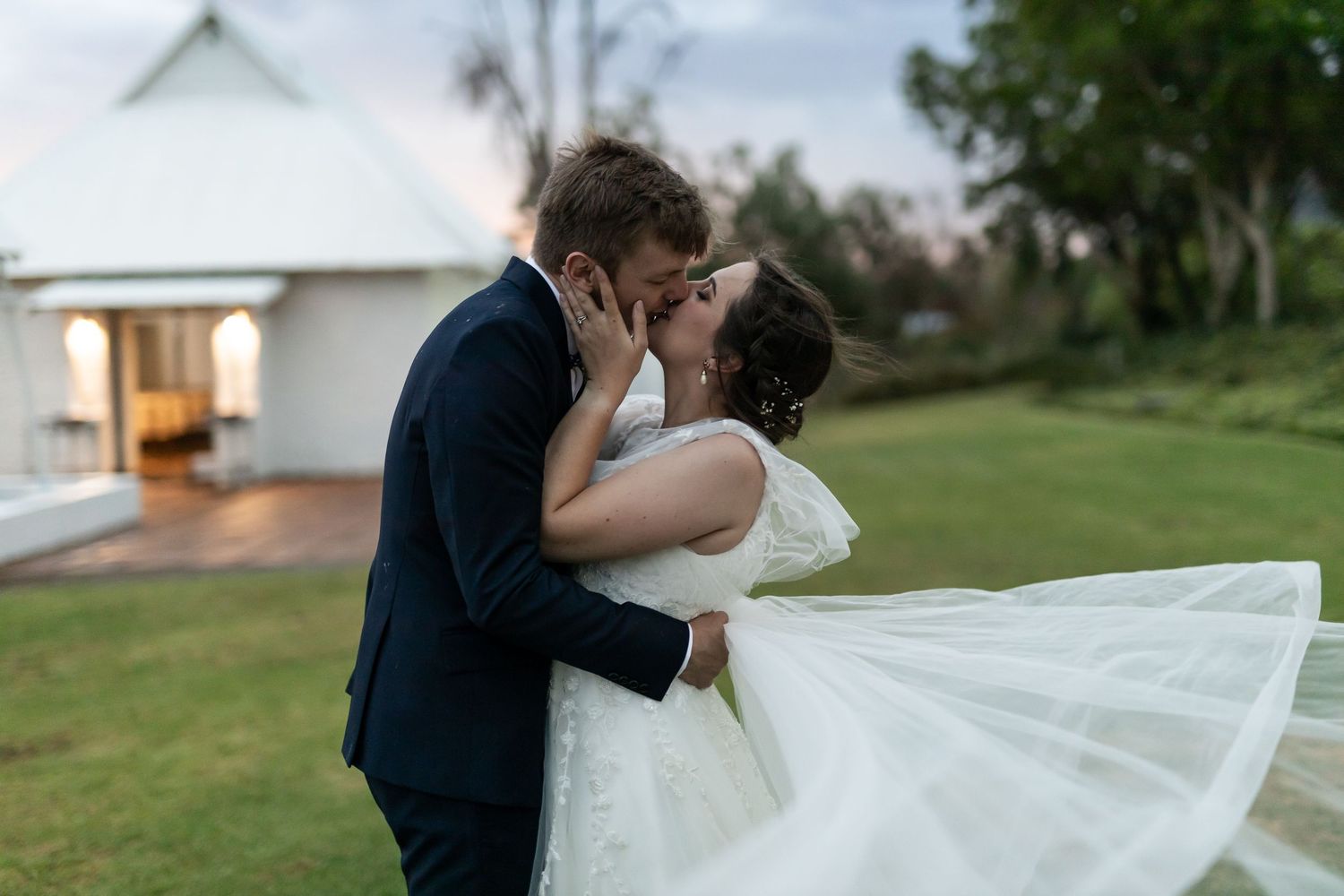 A romantic wedding portrait captured in front of a white chapel with flowing veil details.