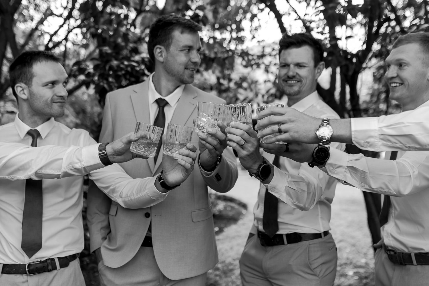 Black and white photo of groomsmen toasting with drinks outdoors.