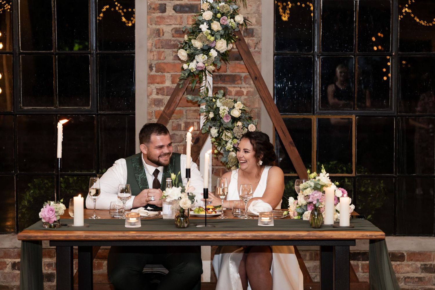 A couple shares an intimate moment at their sweetheart table decorated with floral arrangements.