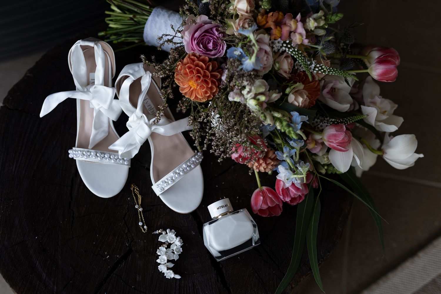 Wedding accessories including white heels and a colorful floral bouquet displayed on dark surface.