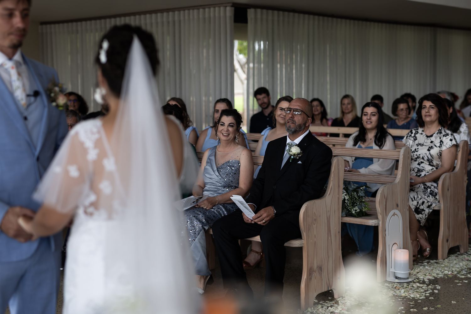Guests watch attentively during an indoor wedding ceremony with natural lighting.