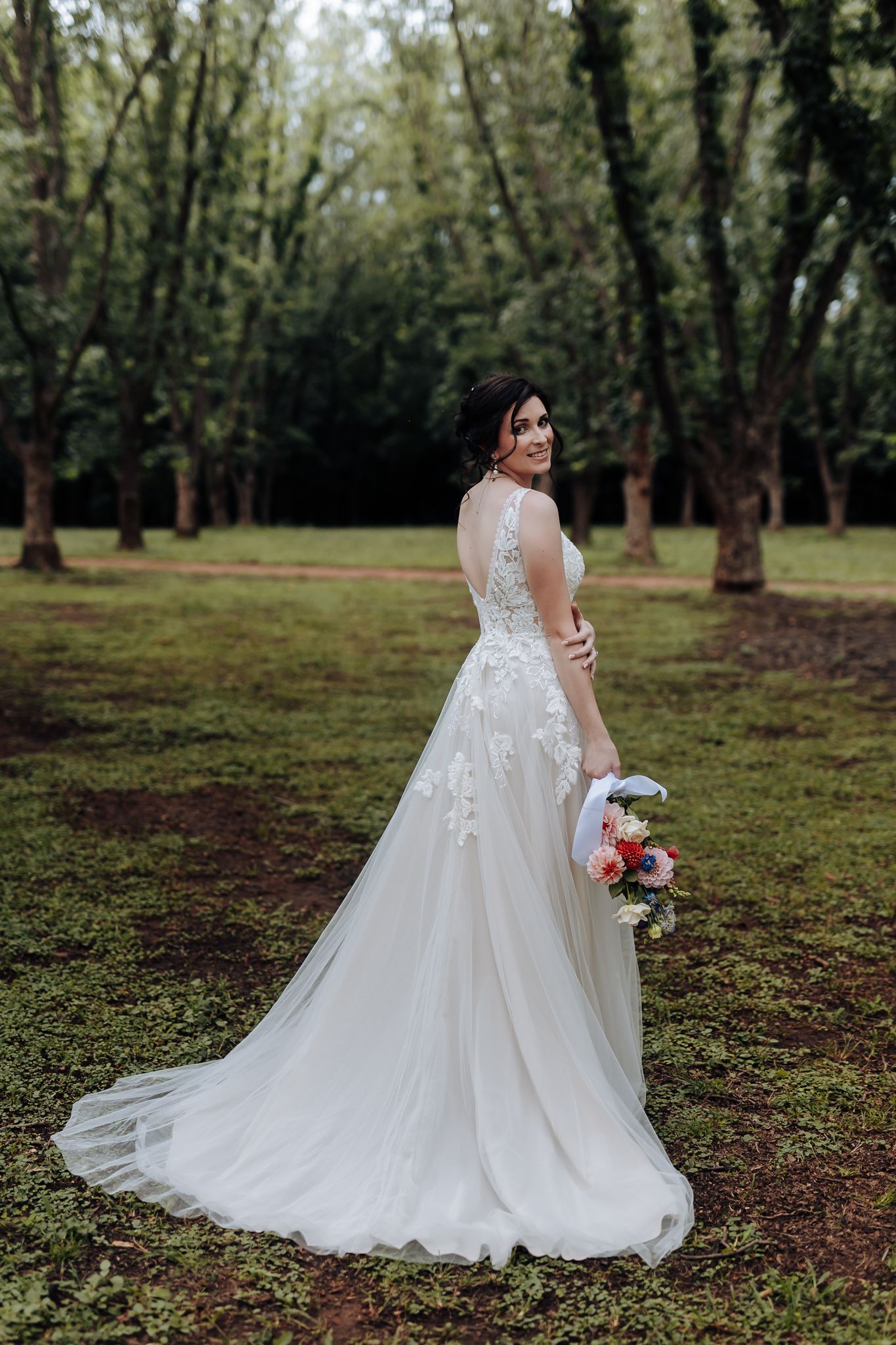 Wedding dress with delicate lace details and flowing train in a forest setting.
