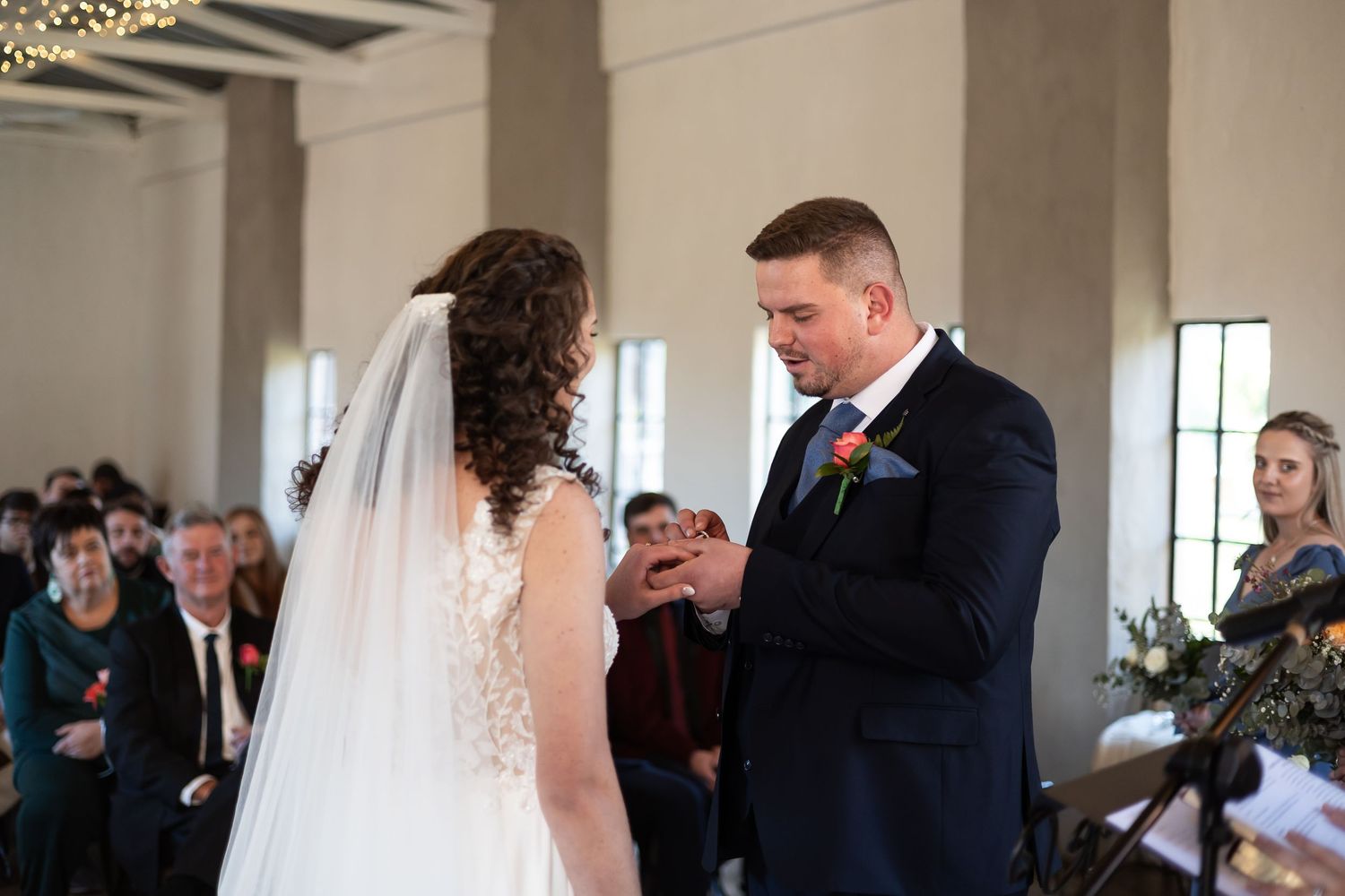 Emotional wedding ceremony moment between bride and groom exchanging vows in front of guests at indoor venue.