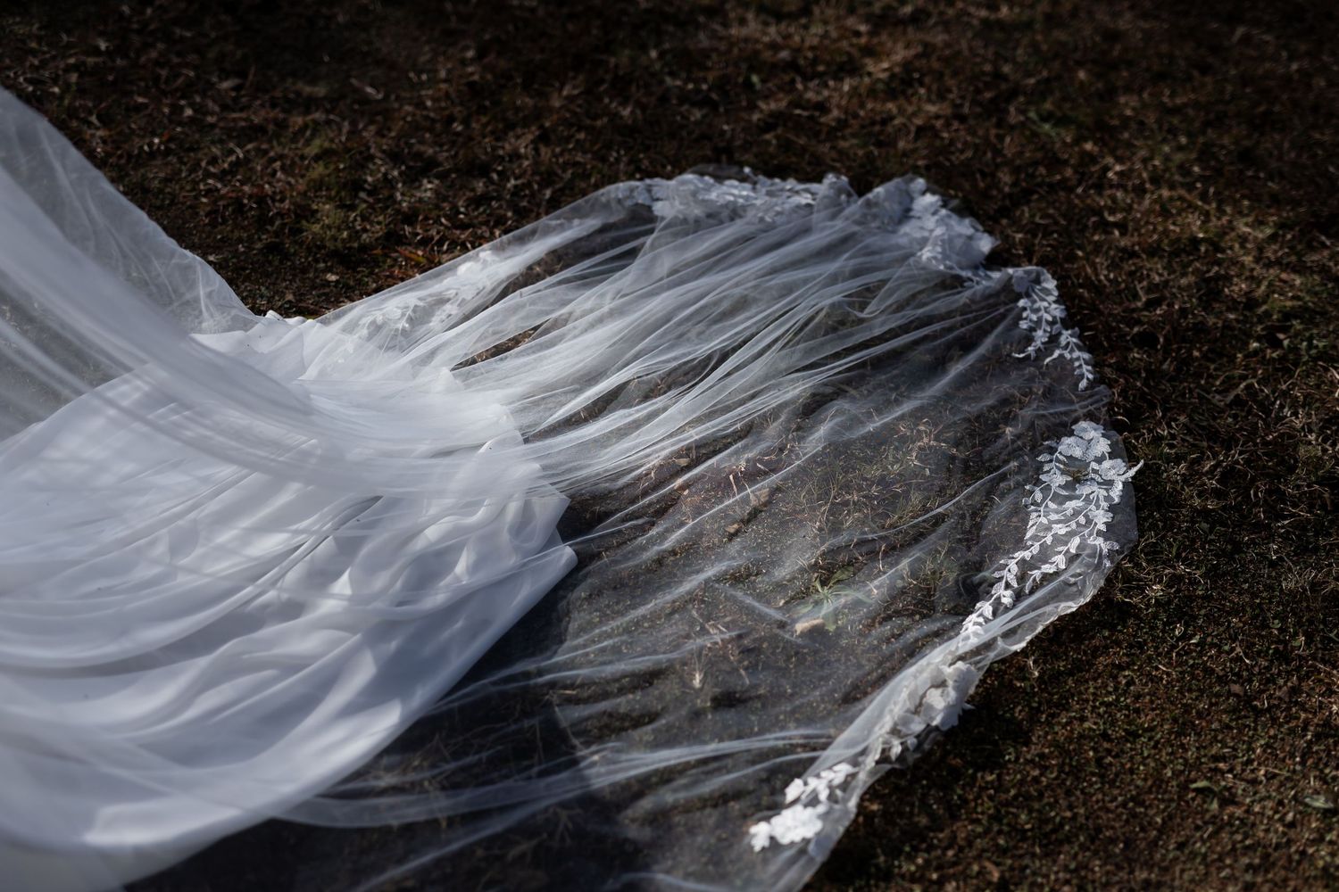 Long flowing white wedding veil being blown beautifully by the wind creating ethereal movement against dark background.
