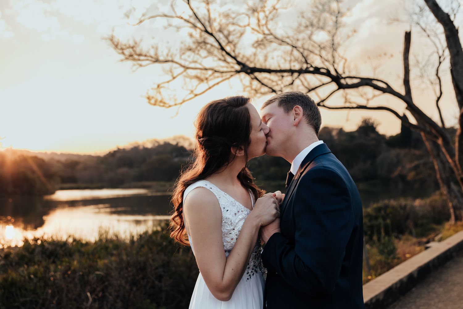 A romantic moment captured at sunset with a lake and trees in the background.